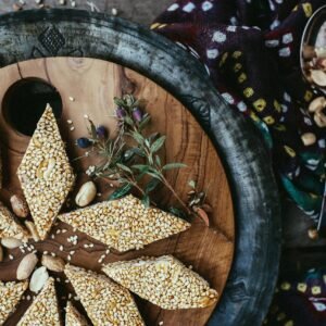 Close-up of sesame and peanut brittle on a wooden serving tray, with rustic decor.